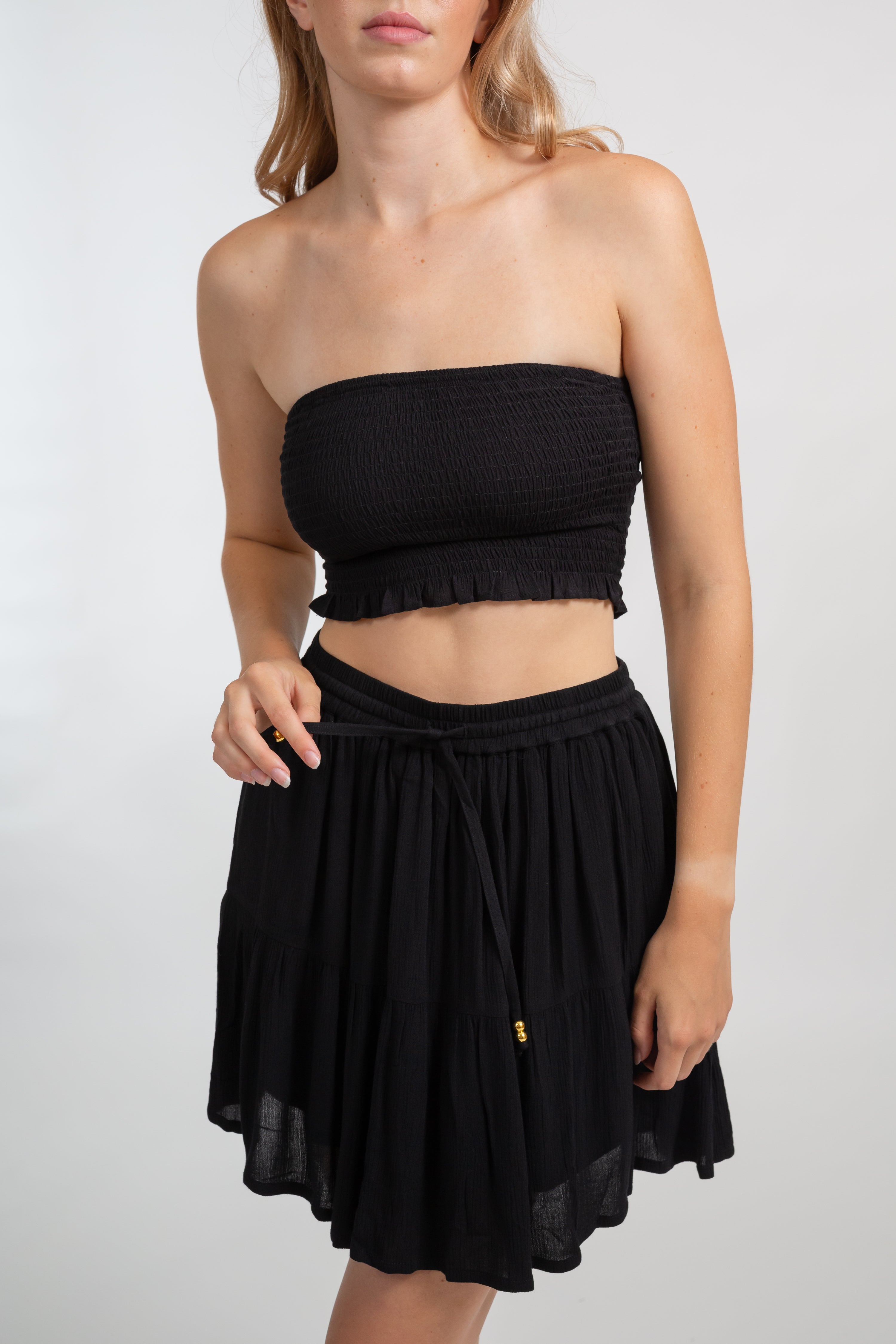 Blonde model facing front close up, wearing Black Miami Smocked Bandeau Top with a smocked elastic chest, cropped style, and bandeau design. Perfect for mixing and matching outfits. Koy Resort affordable vacation, cruise, and resort-wear.