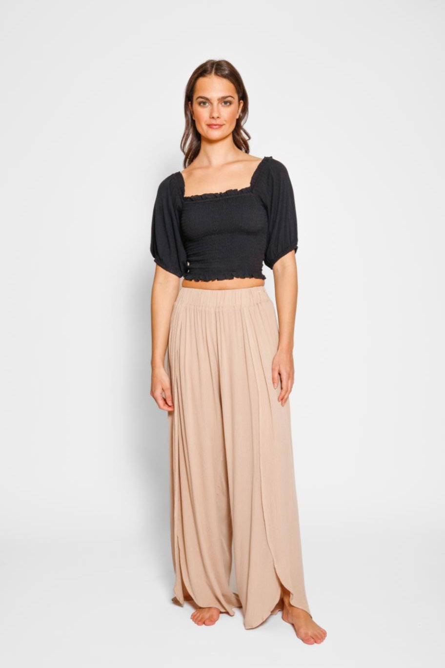 Brunette model facing front, wearing Coconut Beige Miami Split Leg Pants. These beach pants are made of crinkle rayon and feature a relaxed fit with a flowy, true-to-size silhouette. They include an elastic waistband, high side slits, and a rounded hem for a breezy and stylish summer look. Koy Resort affordable vacation, cruise, and resort-wear.